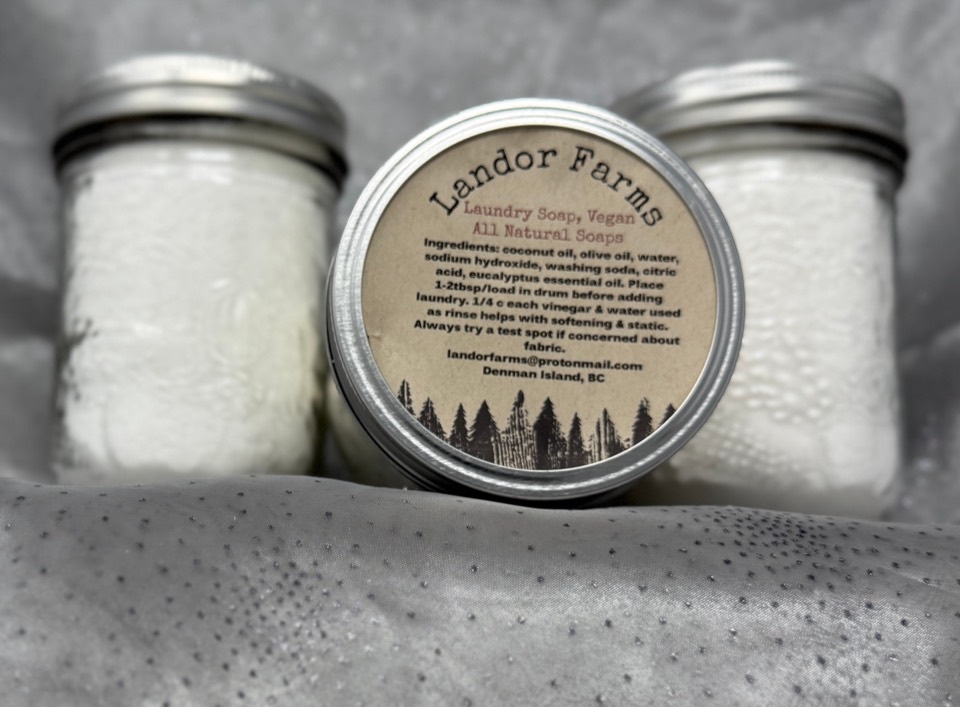 Three jars of white Landor Farms laundry powder with metal lids; the front lid label reads Laundry Soap, Vegan