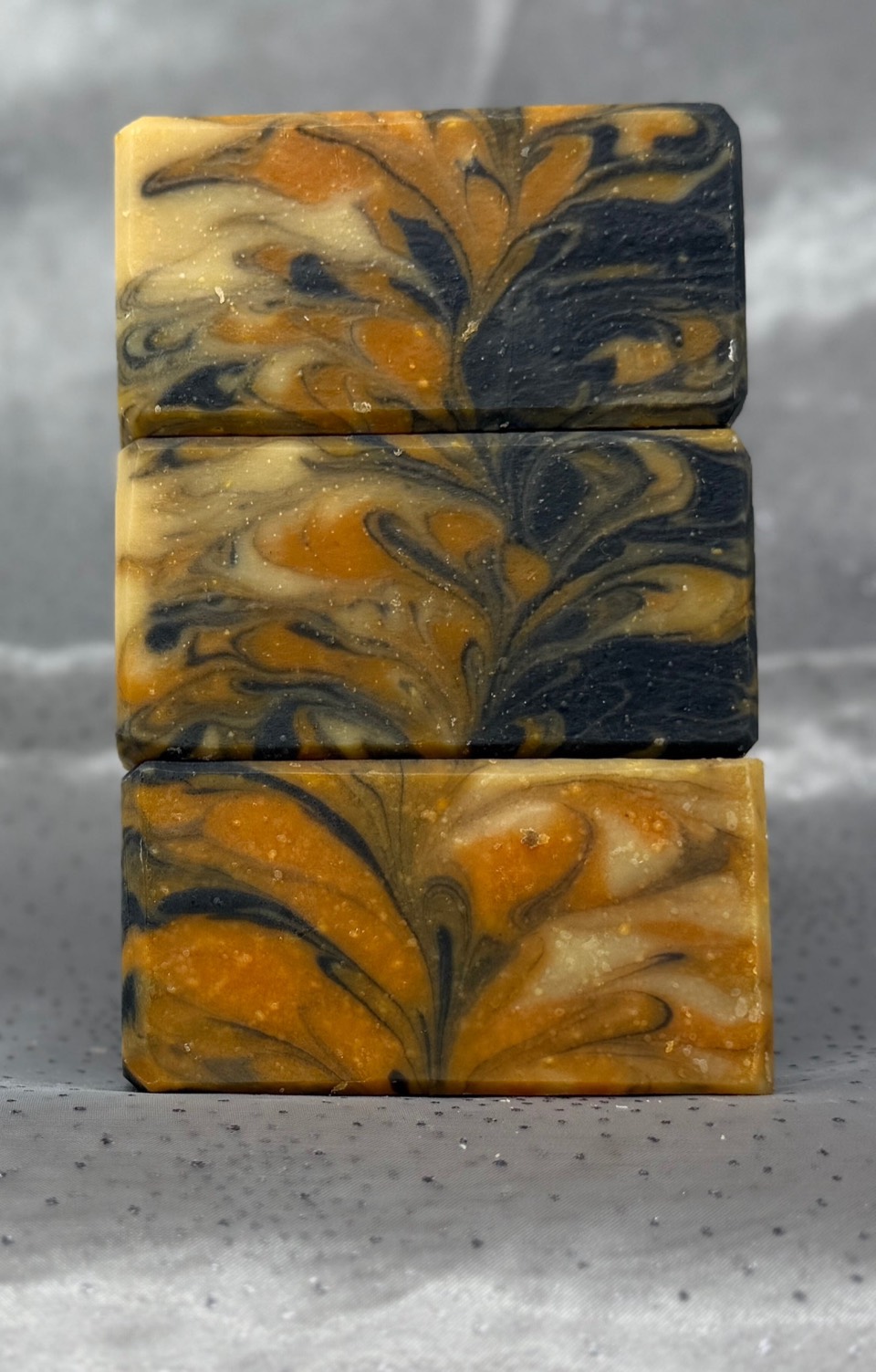 Three stacked Pumpkin Guinness soap bars with orange, cream and black feathered swirls, on grey satin